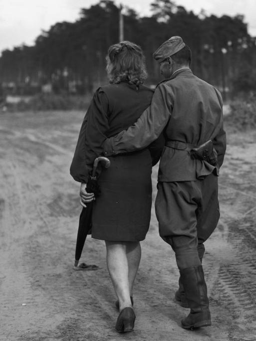Auf dem schwarz-weiß Bild ist ein Paar von hinten abgebildet. Sie gehen von der Kamera weg. Er trägt eine russische Uniform.