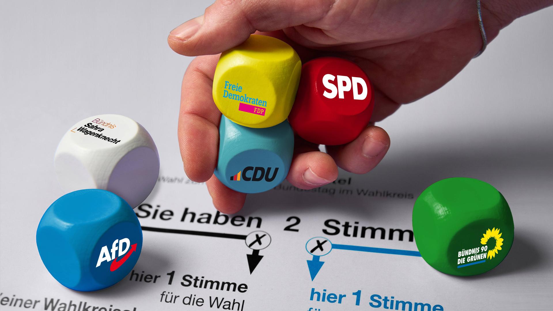 Eine Hand würfelt Würfel von Parteien auf einen Stimm-Zettel.