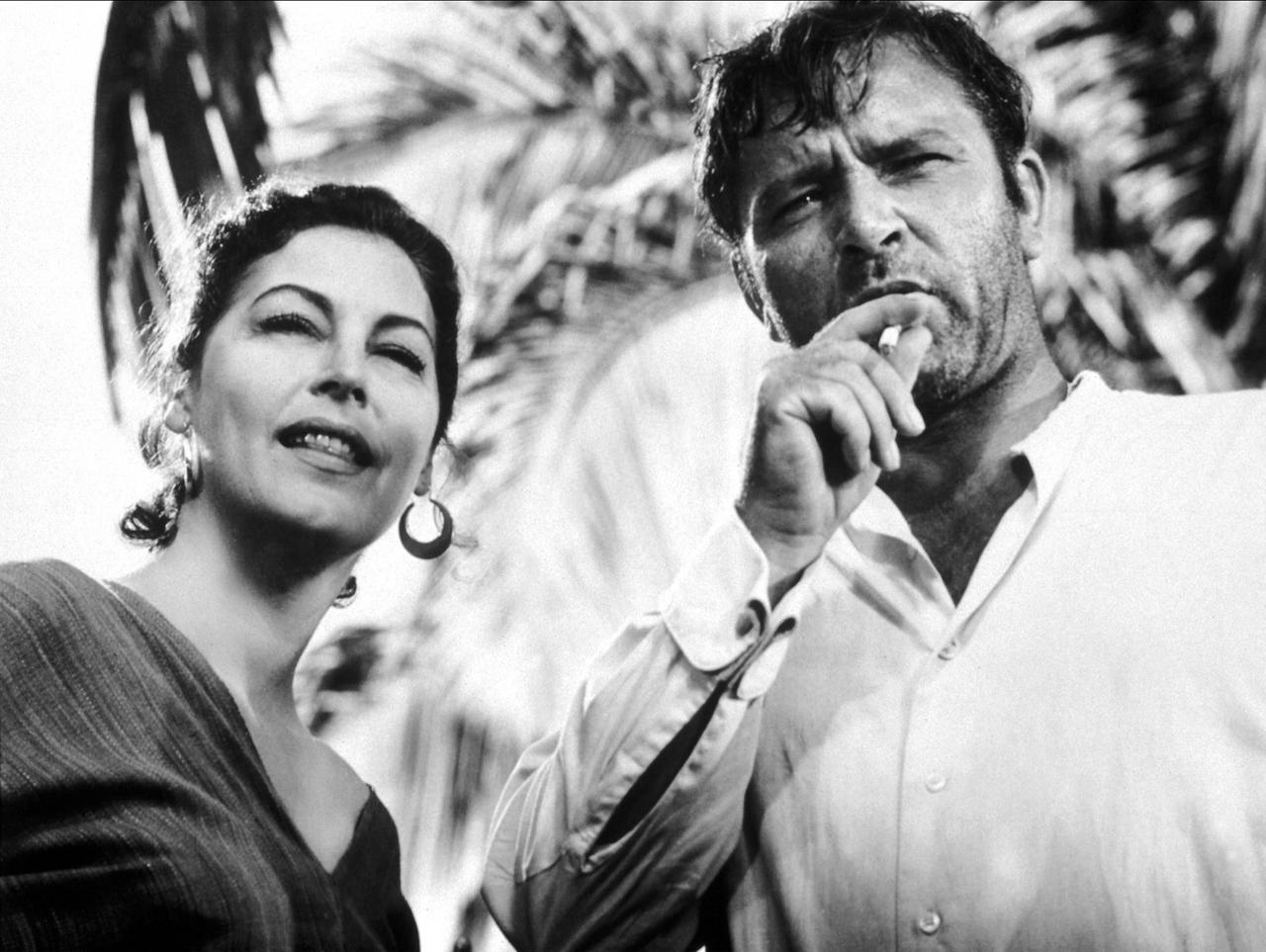 Szene aus dem Film "Die Nacht des Leguan": Ava Gardner und der Zigarette rauchende Richard Burton stehen nebeneinander und schauen nach vorne
