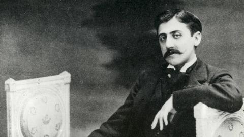 Auf einer alten Fotografie sitzt der Schriftsteller Marcel Proust,leger auf einer Lounge und blickt in die Kamera.