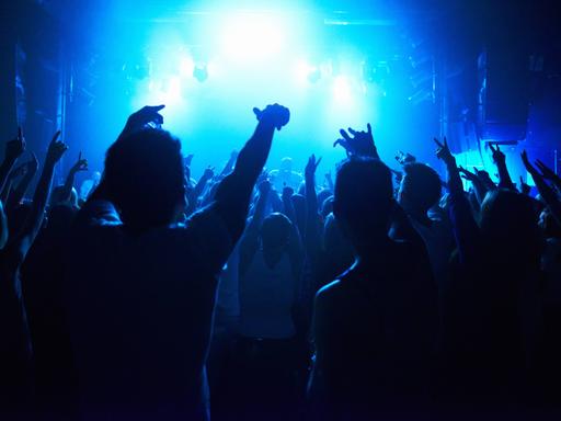 Menschen halten ihre Hände in einem Nachklub nach oben, um sie herum blaues Licht und Nebel