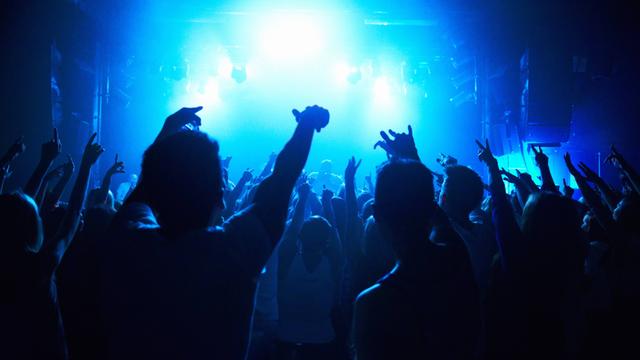 Menschen halten ihre Hände in einem Nachklub nach oben, um sie herum blaues Licht und Nebel