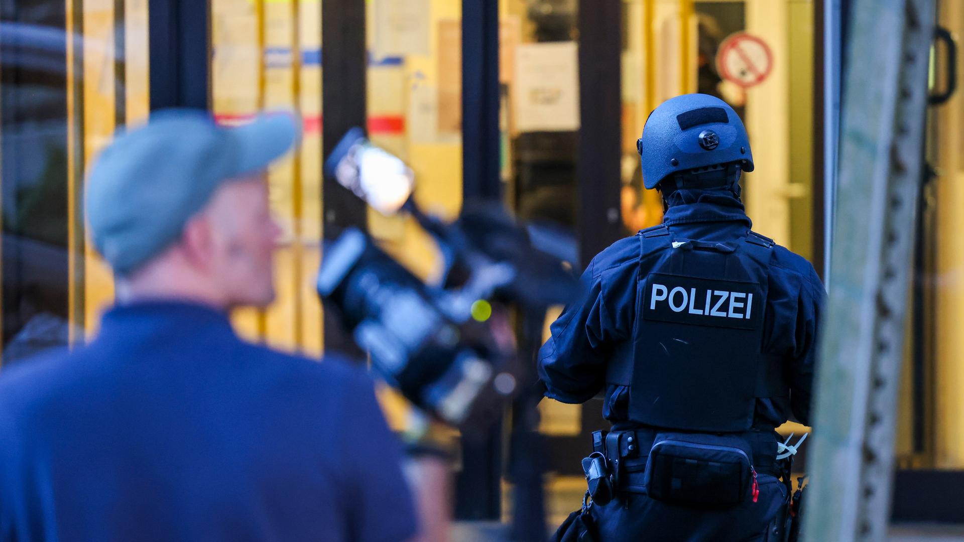 Im Fokus ist ein Polizist, verschwommen im Vordergrund ist ein Kameramann zu sehen.