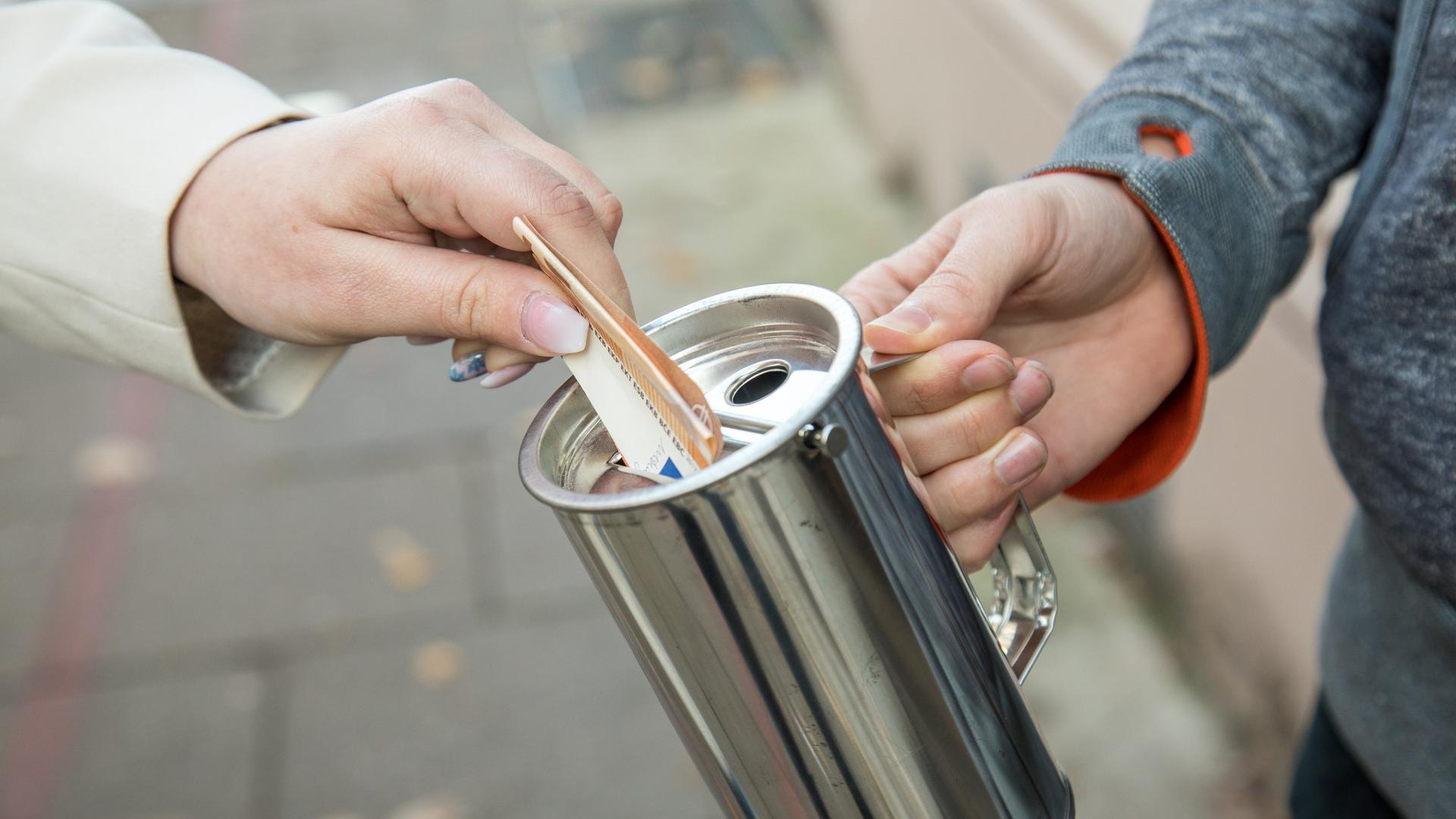 Eine Hand hält eine Spendenbüchse, eine andere steckt einen Euroschein hinein Eine Hand hält eine Spendenbüchse, eine andere steckt einen Euroschein hinein
