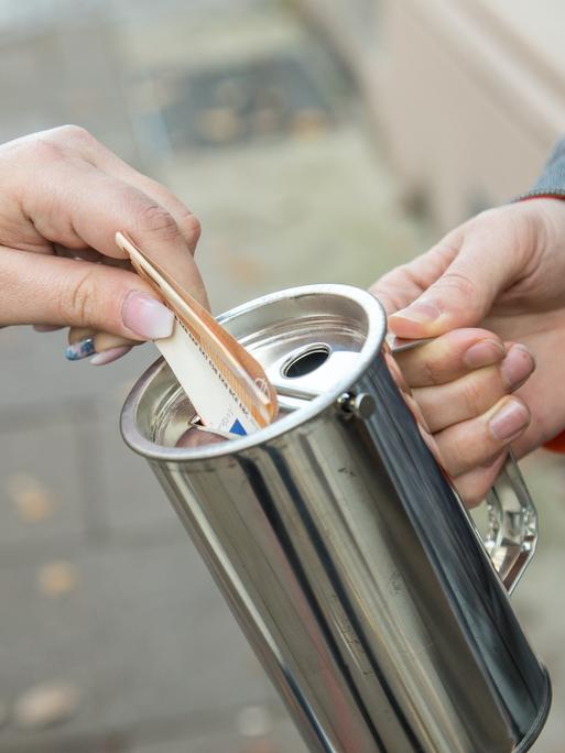 Eine Hand hält eine Spendenbüchse, eine andere steckt einen Euroschein hinein Eine Hand hält eine Spendenbüchse, eine andere steckt einen Euroschein hinein