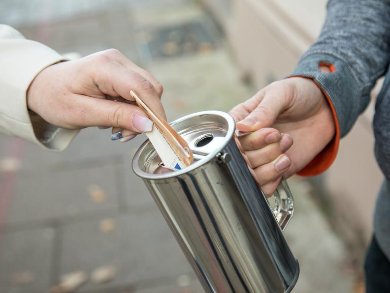Eine Hand hält eine Spendenbüchse, eine andere steckt einen Euroschein hinein Eine Hand hält eine Spendenbüchse, eine andere steckt einen Euroschein hinein