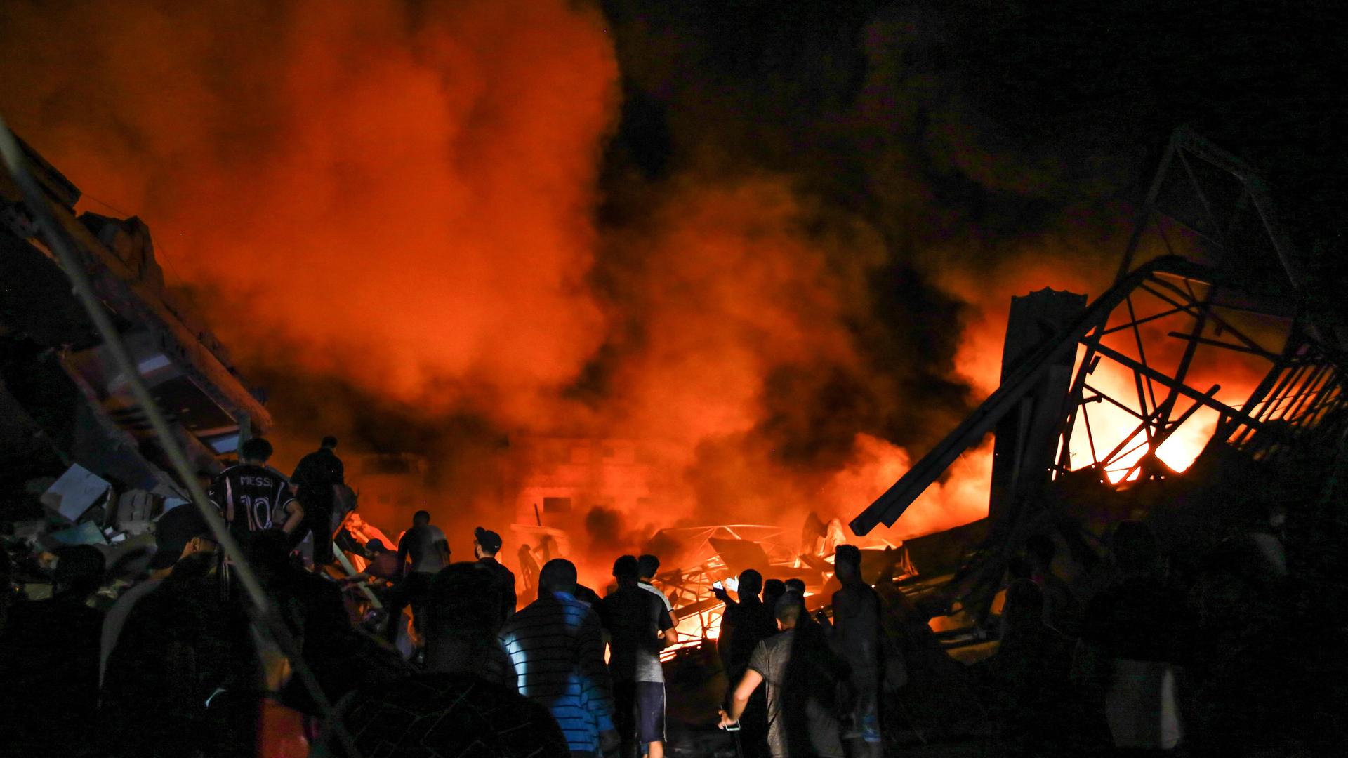 Leute stehen vor einem Haus, aus dem Rauch und Feuer nach einem israelischen Angriff im Gazastreifen aufsteigt Leute stehen vor einem Haus, aus dem Rauch und Feuer nach einem israelischen Angriff im Gazastreifen aufsteigt
