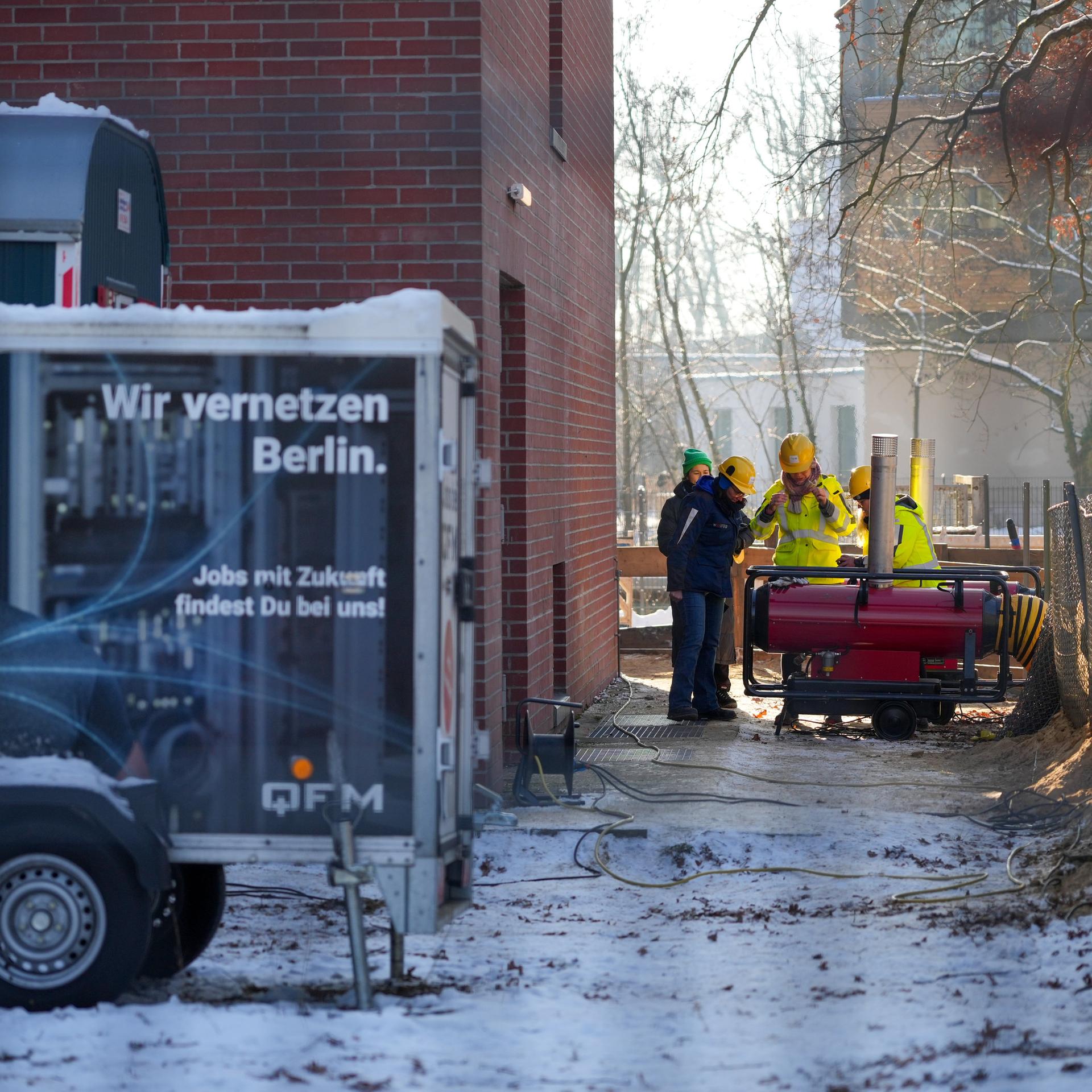 Mehrere Mitarbeiter des Umspannwerkes an der Argentinischen Allee stehen hinter einem Zaun nebeneinander. Im Vordergrund steht ein Anhänger mit der Aufschrift "Wir vernetzen Berlin". 