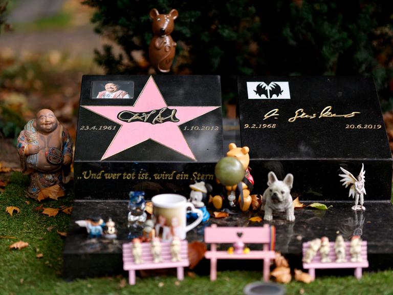 Das Grab von Entertainer Dirk Bach auf dem Melaten-Friedhof: Immer wieder bringen Fans kleine Figürchen vorbei oder haben auf einer rosa Bank am Grab eine 'Audienz beim Mausekönig'. Die Stadt Köln ließ alle Bänke entfernen.