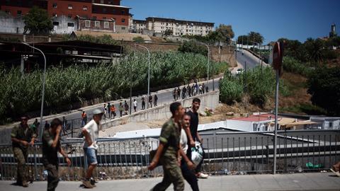 Eine Gruppe Migranten wird von spanischen Soldaten eine Straße entlang zurück nach Marokko eskortiert.