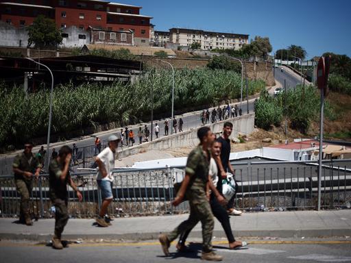 Eine Gruppe Migranten wird von spanischen Soldaten eine Straße entlang zurück nach Marokko eskortiert. Eine Gruppe Migranten wird von spanischen Soldaten eine Straße entlang zurück nach Marokko eskortiert.