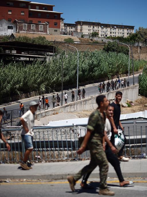 Eine Gruppe Migranten wird von spanischen Soldaten eine Straße entlang zurück nach Marokko eskortiert. Eine Gruppe Migranten wird von spanischen Soldaten eine Straße entlang zurück nach Marokko eskortiert.