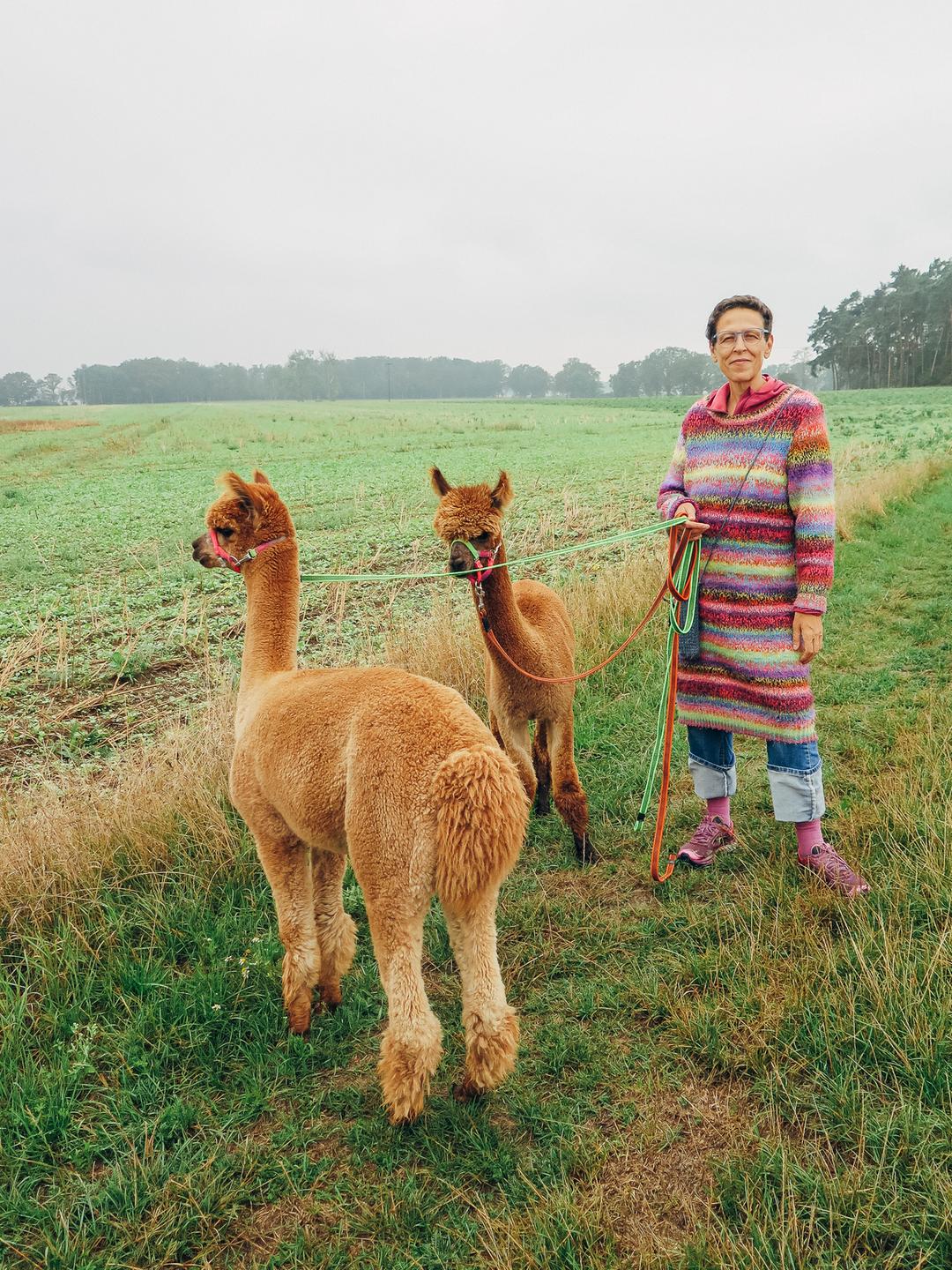 Schirin Schahbaz steht mit zwei ihrer Alpakas auf einem Feld.