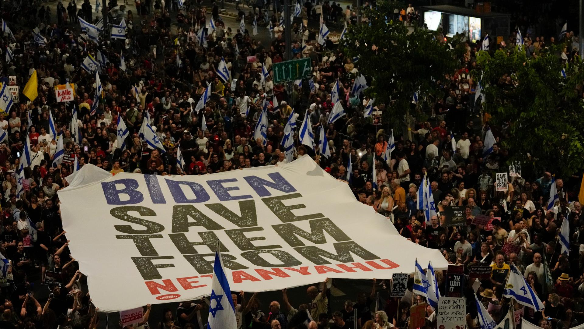 Menschen protestieren in Tel Aviv gegen die Regierung von Premierminister Benjamin Netanjahu. Die Demonstranten fordern von der Hamas die Freilassung der Geiseln. Auf einem Transparenz bitten sie um Vermittlung von US-Präsident Biden. 
