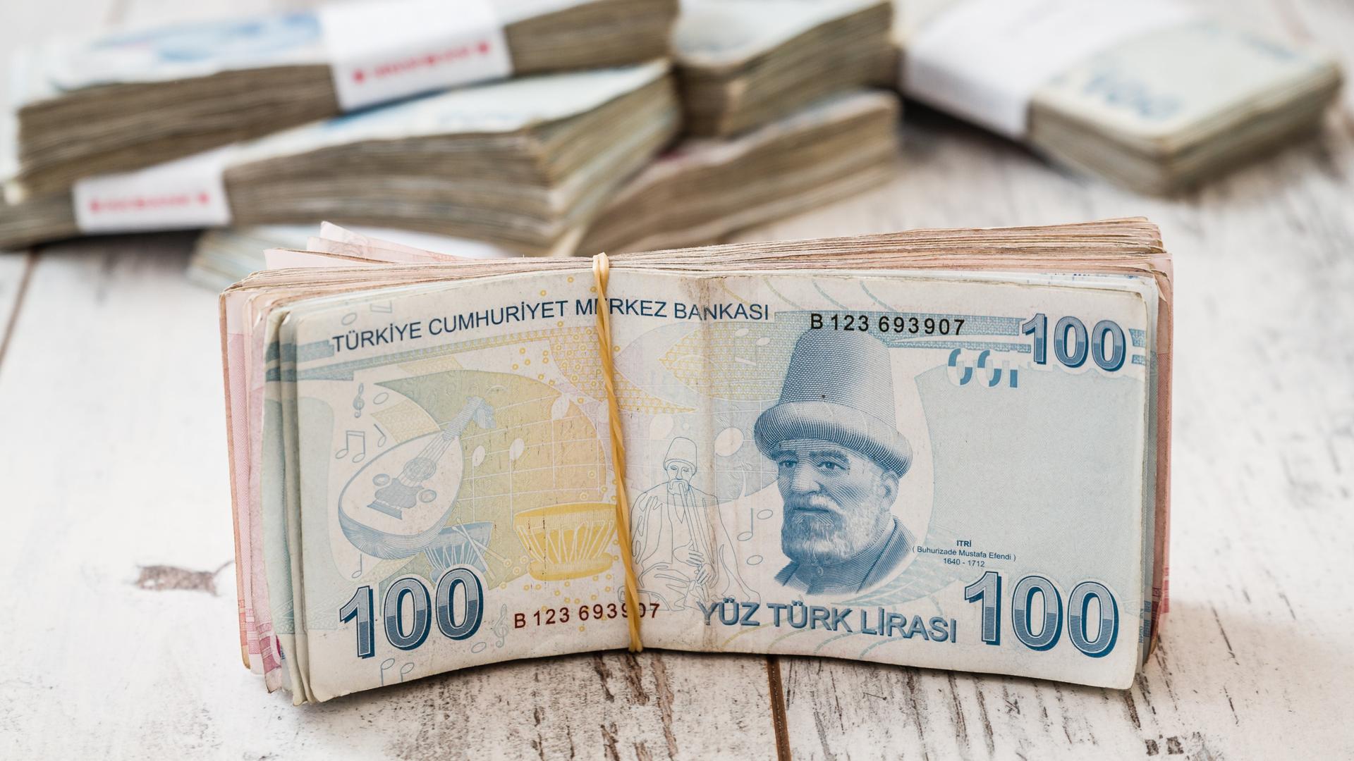 Ein Bündel 100 Lira Scheine liegt auf weisser Holzoberfläche.