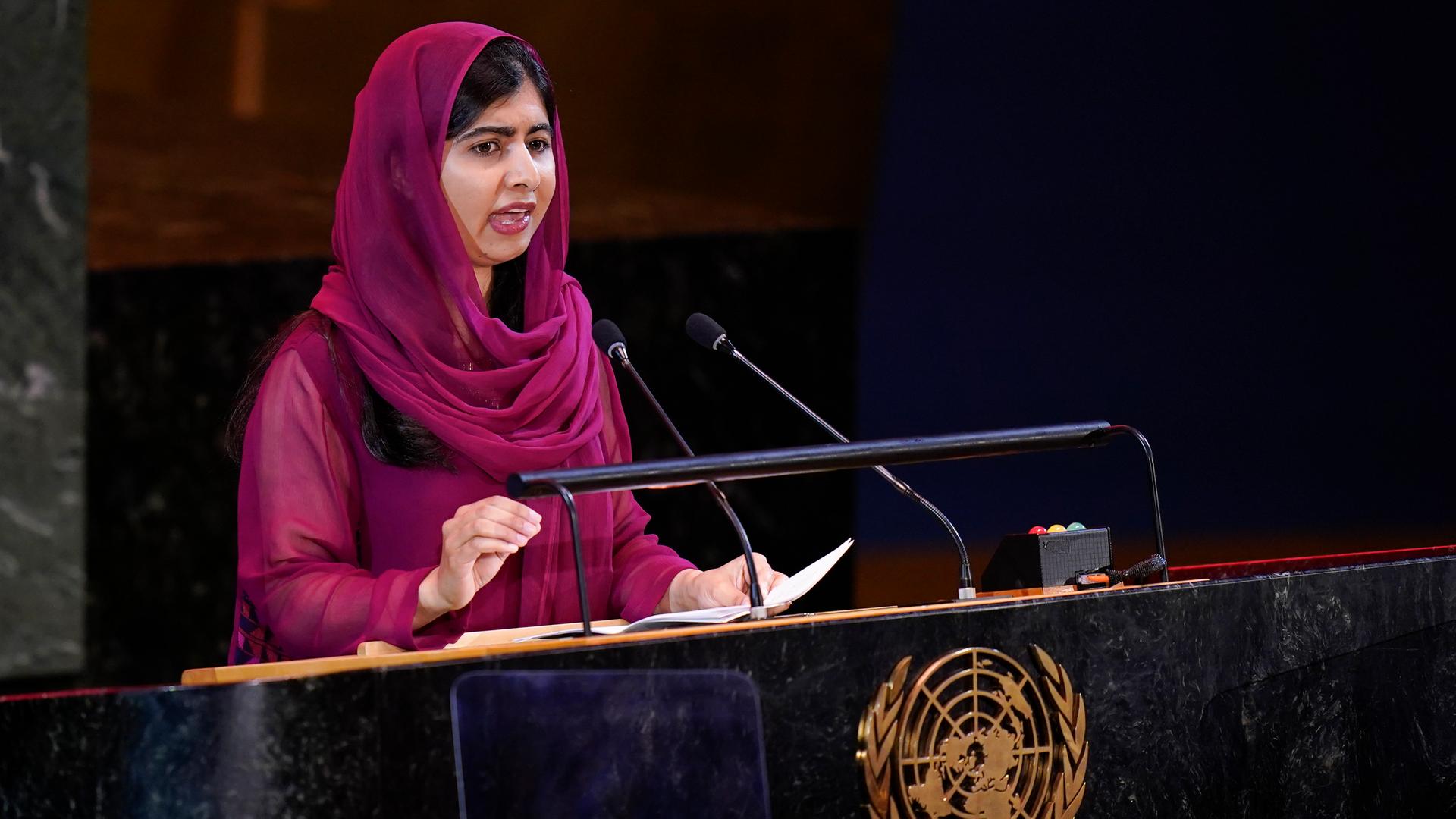 Das Bild zeigt die Friedensnobelpreisträgerin Malala Yousafzai . Sie steht vor einem Pult und hält eine Rede.