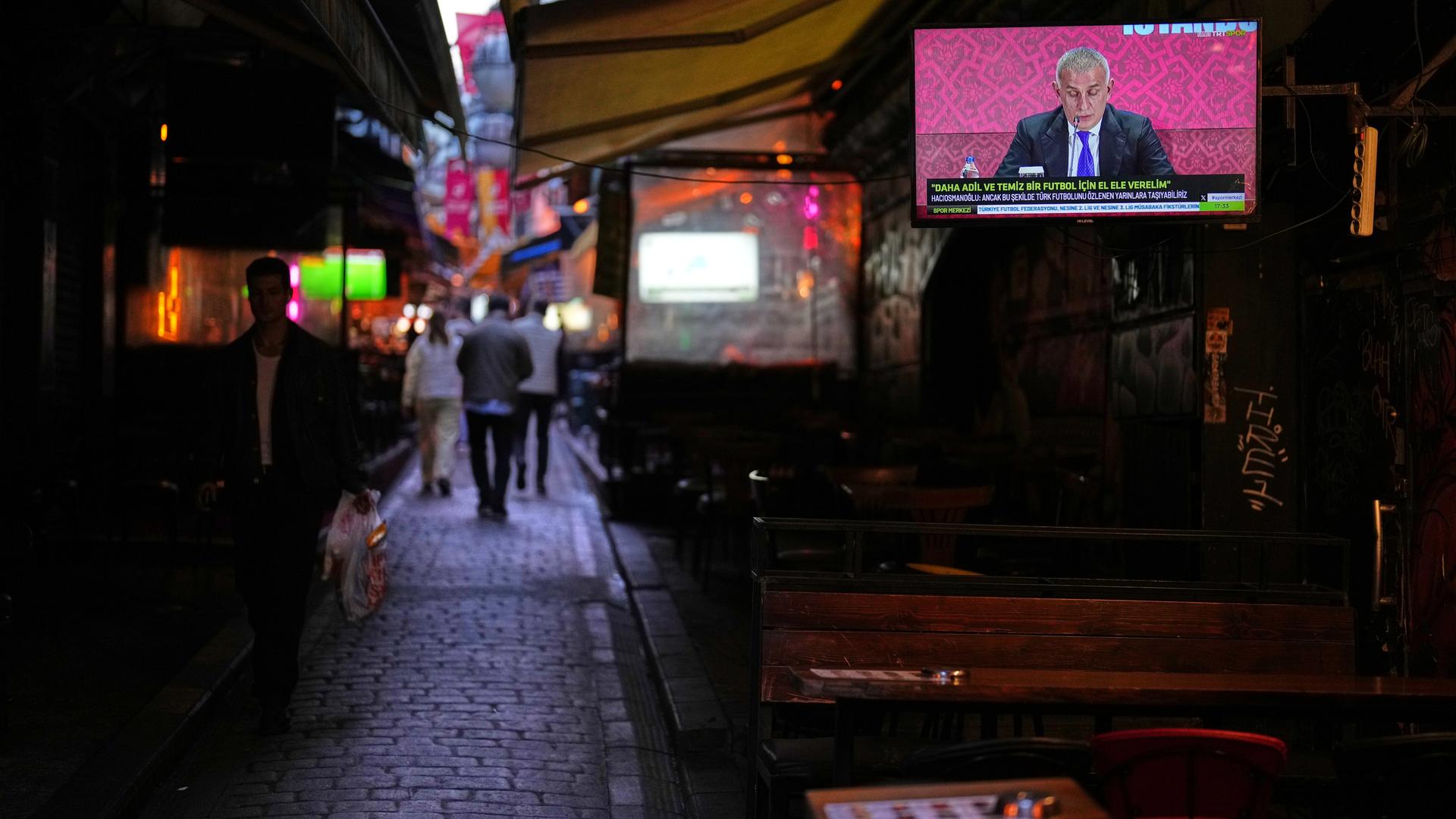 Istanbul: Menschen gehen an einem Fernsehbildschirm vorbei, auf dem der Präsident des Türkischen Fußballverbands, Ibrahim Haciosmanoglu, während einer Pressekonferenz zu sehen ist. 