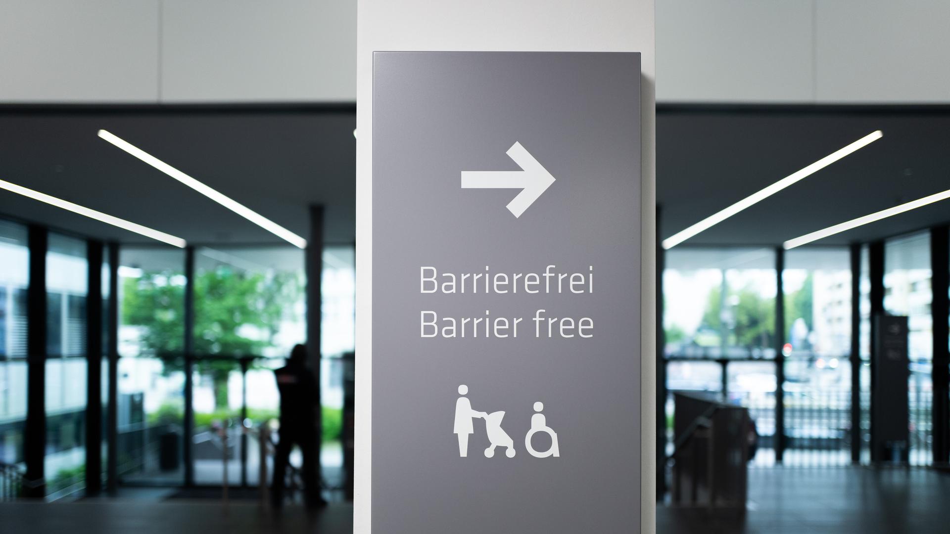 Schild mit einem Pfeil und Symbolen für eine Frau mit Kinderwagen und einen Rollstuhlfahrer sowie der Aufschrift "Barrierefrei - Barrier free"