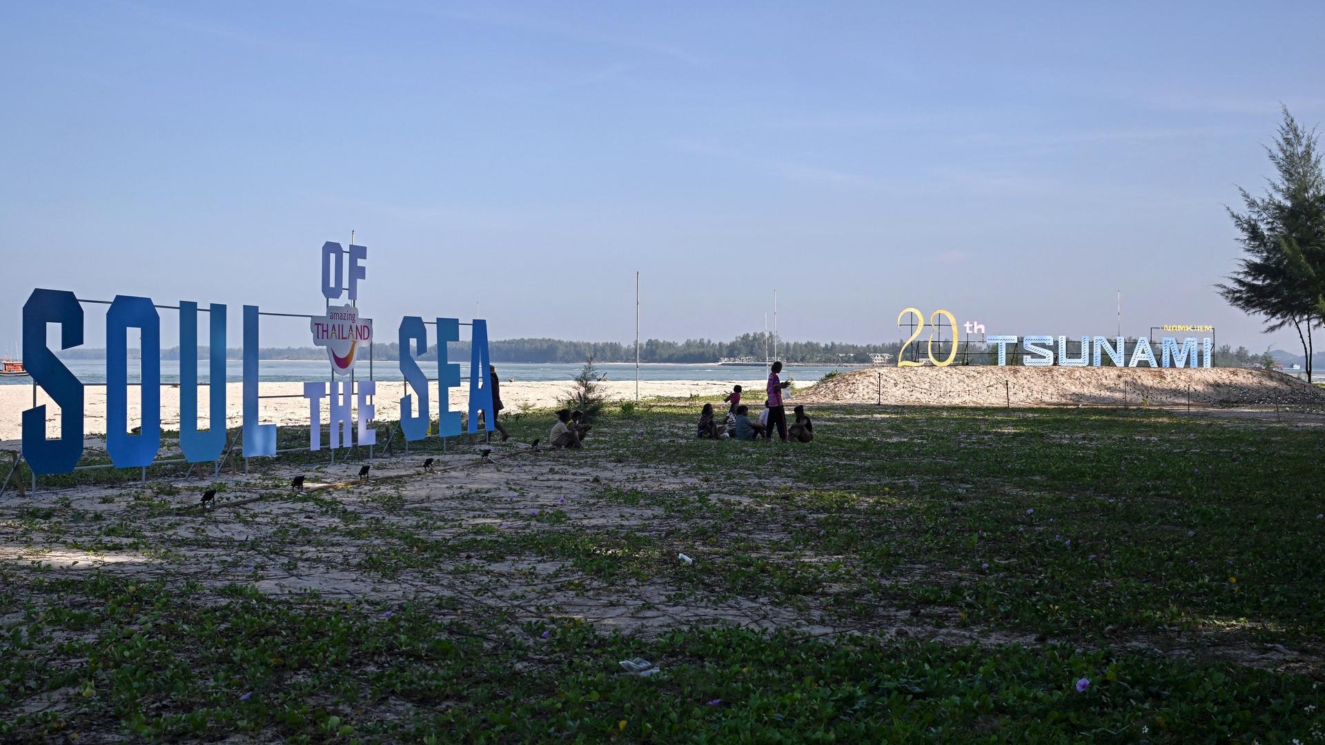 Menschen am Strand in der thailändischen Provinz Phang Nga zwischen großen Schriftzügen, die an den Tsunami von 2004 erinnern - December 26, 2024. (Photo by Lillian SUWANRUMPHA / AFP)
