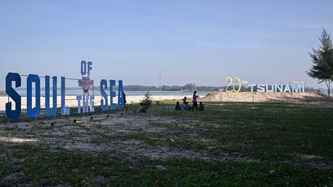 Menschen am Strand in der thailändischen Provinz Phang Nga zwischen großen Schriftzügen, die an den Tsunami von 2004 erinnern - December 26, 2024. (Photo by Lillian SUWANRUMPHA / AFP)