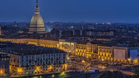 Die erleuchtete Stadt Turin bei Nacht, über der die Mole Antonelliana thront. Der pavillonartige Bau mit seinem hohen, sich stark verjüngenden Aufsatz ist das Wahrzeichen der Stadt.