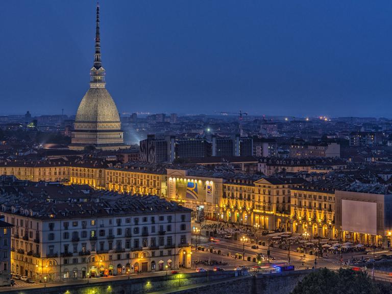 Die erleuchtete Stadt Turin bei Nacht, über der die Mole Antonelliana thront. Der pavillonartige Bau mit seinem hohen, sich stark verjüngenden Aufsatz ist das Wahrzeichen der Stadt.