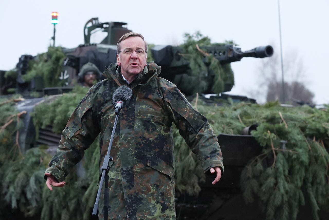 Bundesverteidigungsminister Pistorius steht in Tarnkleidung vor einem Mikrofon. Hinter ihm ein getarnter Panzer. v
