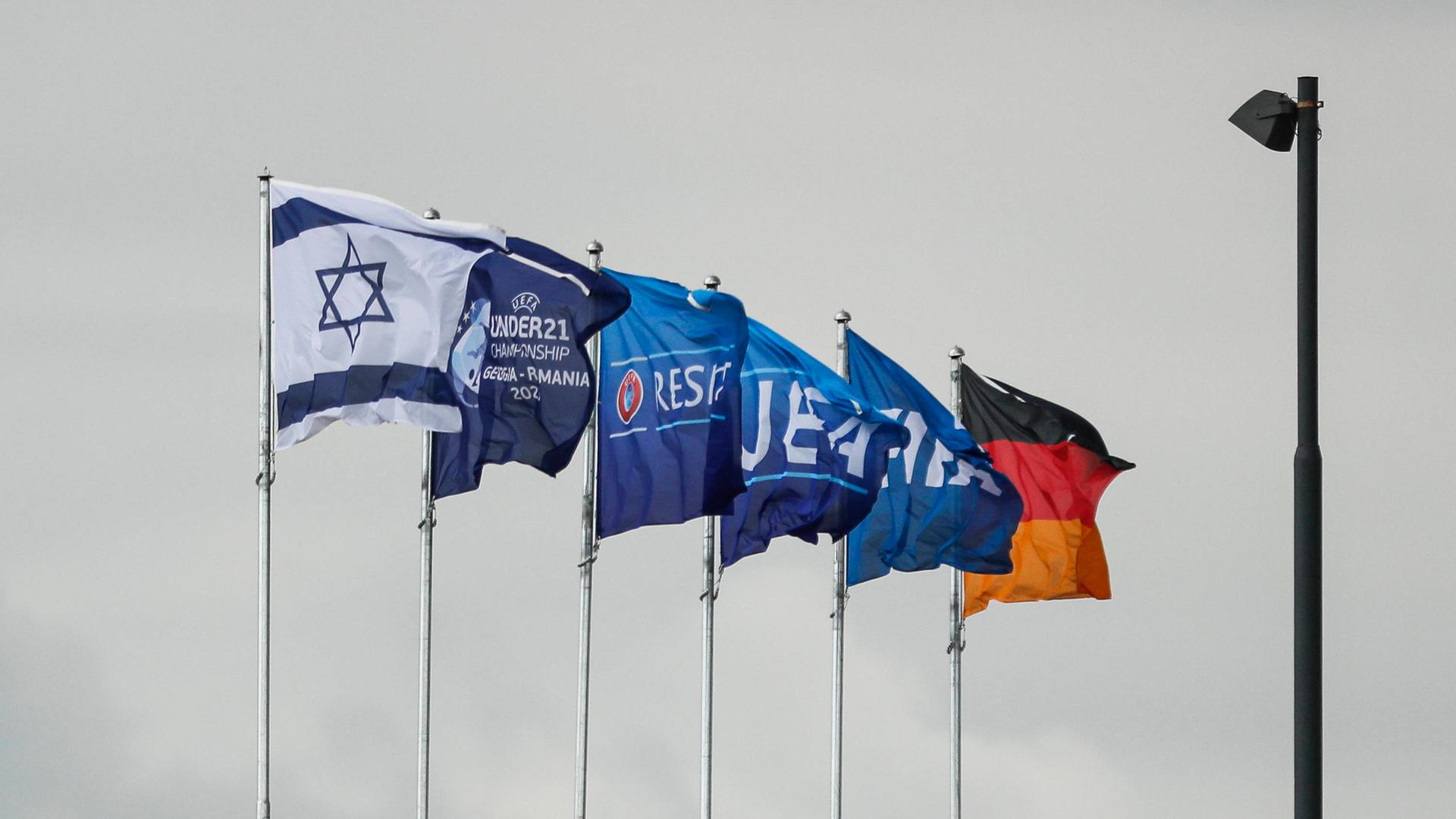 Die Flaggen Israels, Deutschlands und der UEFA wehen am Stadion in Georgien. Im Hintergrund grauer Himmel.