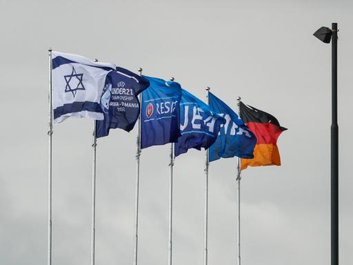 Die Flaggen Israels, Deutschlands und der UEFA wehen am Stadion in Georgien. Im Hintergrund grauer Himmel.