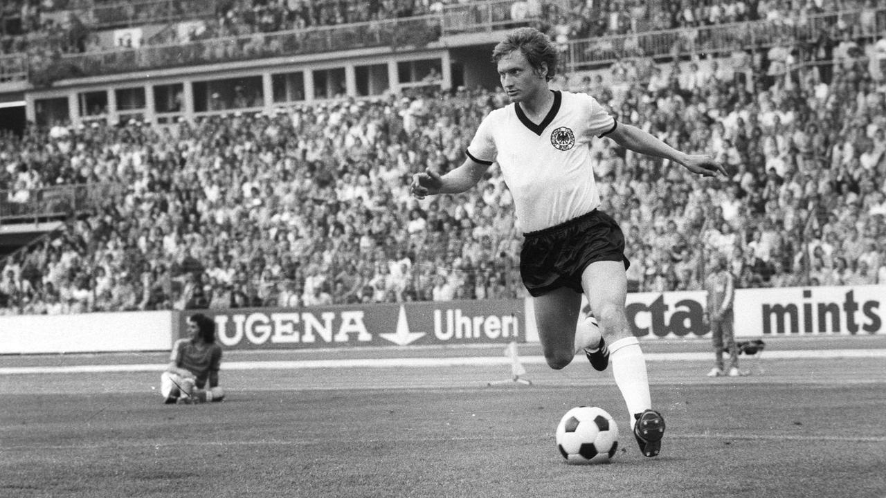 Dieter Herzog tritt den Ball auf einem Schwarz-Weiß-Bild in vollem Stadion.