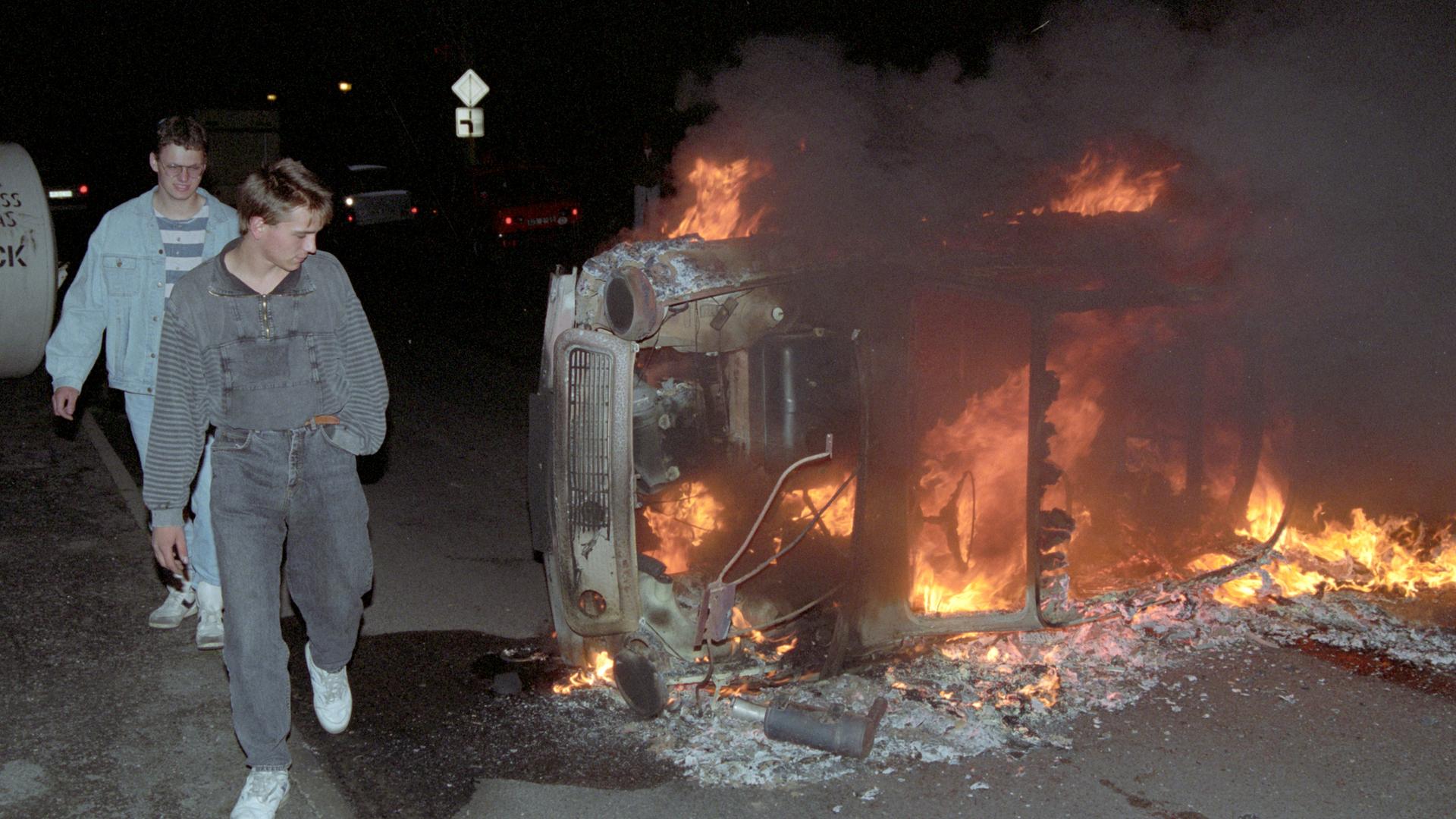 Rassistische Krawalle Rostock-Lichtenhagen 1992: Jugendliche laufen in der Nacht zum 27.08.1992 in Rostock-Lichtenhagen an einem umgestürzten und von rechtsradikalen Randalierern in Brand gesetzten Pkw Tranbant vorbei. 