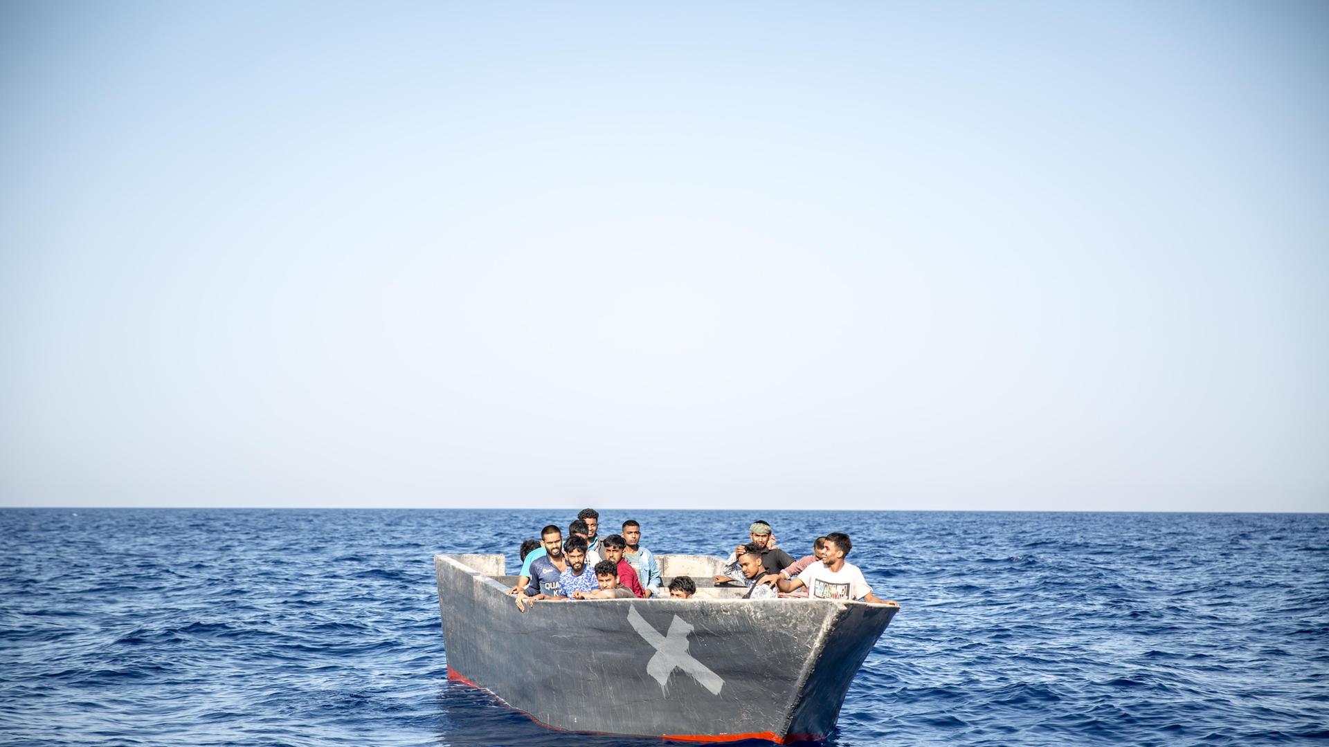 Menschen sitzen in einem Holzboot, das auf dem Mittelmeer treibt. (3. August 2024)