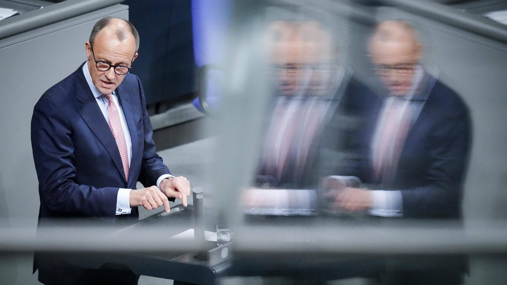 Friedrich Merz, CDU-Bundesvorsitzender und Unionsfraktionsvorsitzender, spricht im Bundestag, er spiegelt sich selbst noch zweimal verschwommen im Bild