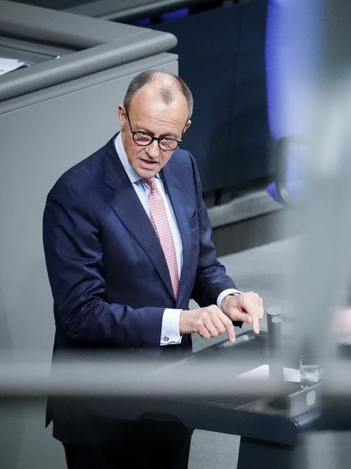 Friedrich Merz, CDU-Bundesvorsitzender und Unionsfraktionsvorsitzender, spricht im Bundestag, er spiegelt sich selbst noch zweimal verschwommen im Bild