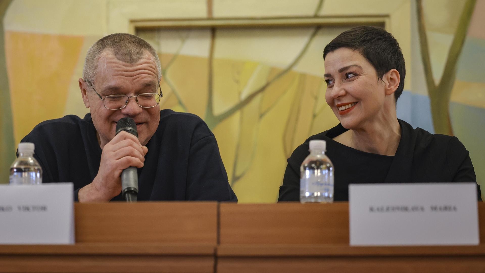 Auf einer Pressekonferenz am 14.12.2025 schaut Maria Kolesnikowa lächelnd zu ihrem Sitznachbar Viktor Babariko, der in ein Mikro spricht Auf einer Pressekonferenz am 14.12.2025 schaut Maria Kolesnikowa lächelnd zu ihrem Sitznachbar Viktor Babariko, der in ein Mikro spricht