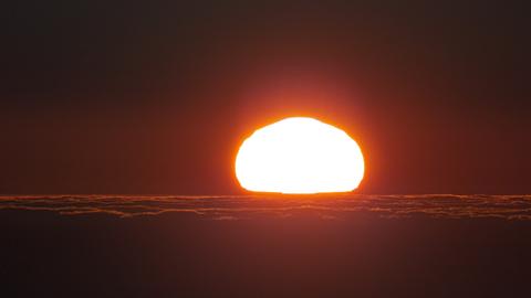 Gleißender Sonnenuntergang vor dunklem Horizont