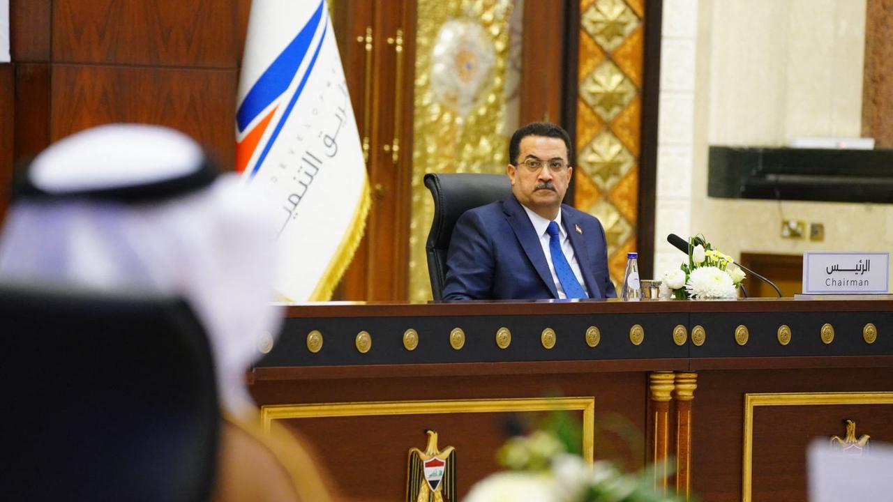 Der irakische Ministerpräsident al-Sudani sitzt hinter einem großen Tisch vor einer Flagge.