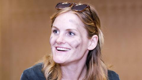 Eine Frau Anfang 30 im Porträt: Cey Leonard hat lange Haare, hat eine Sonnenbrille ins Haar gesteckt und schwarze Streifen auf die Wangen gemalt.