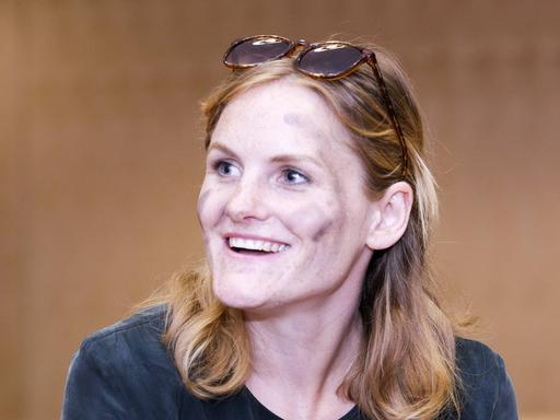 Eine Frau Anfang 30 im Porträt: Cey Leonard hat lange Haare, hat eine Sonnenbrille ins Haar gesteckt und schwarze Streifen auf die Wangen gemalt.