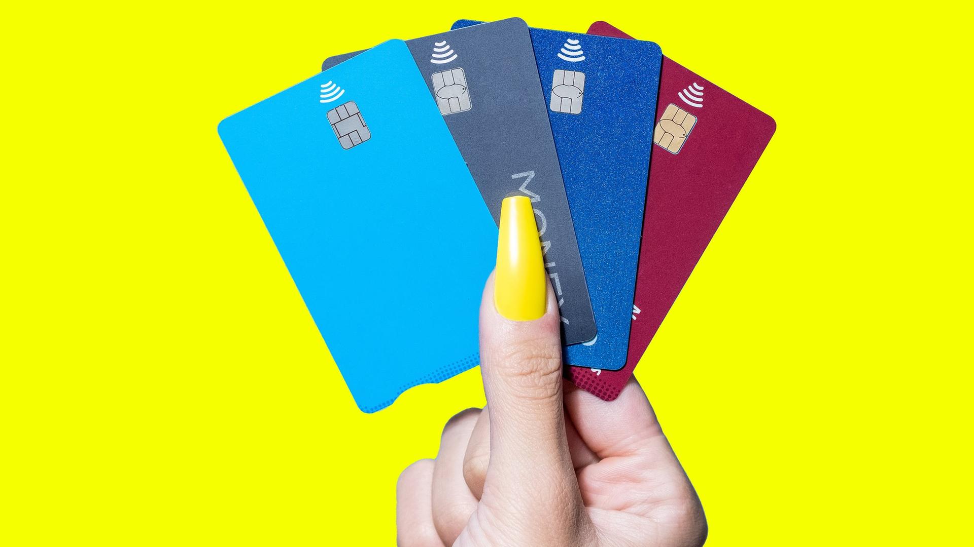 Mehrere Kreditkarten, die von einer Hand mit einem auffälligen gelben Fingernagel gehalten werden.
