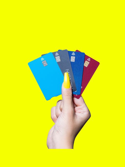 Mehrere Kreditkarten, die von einer Hand mit einem auffälligen gelben Fingernagel gehalten werden.
