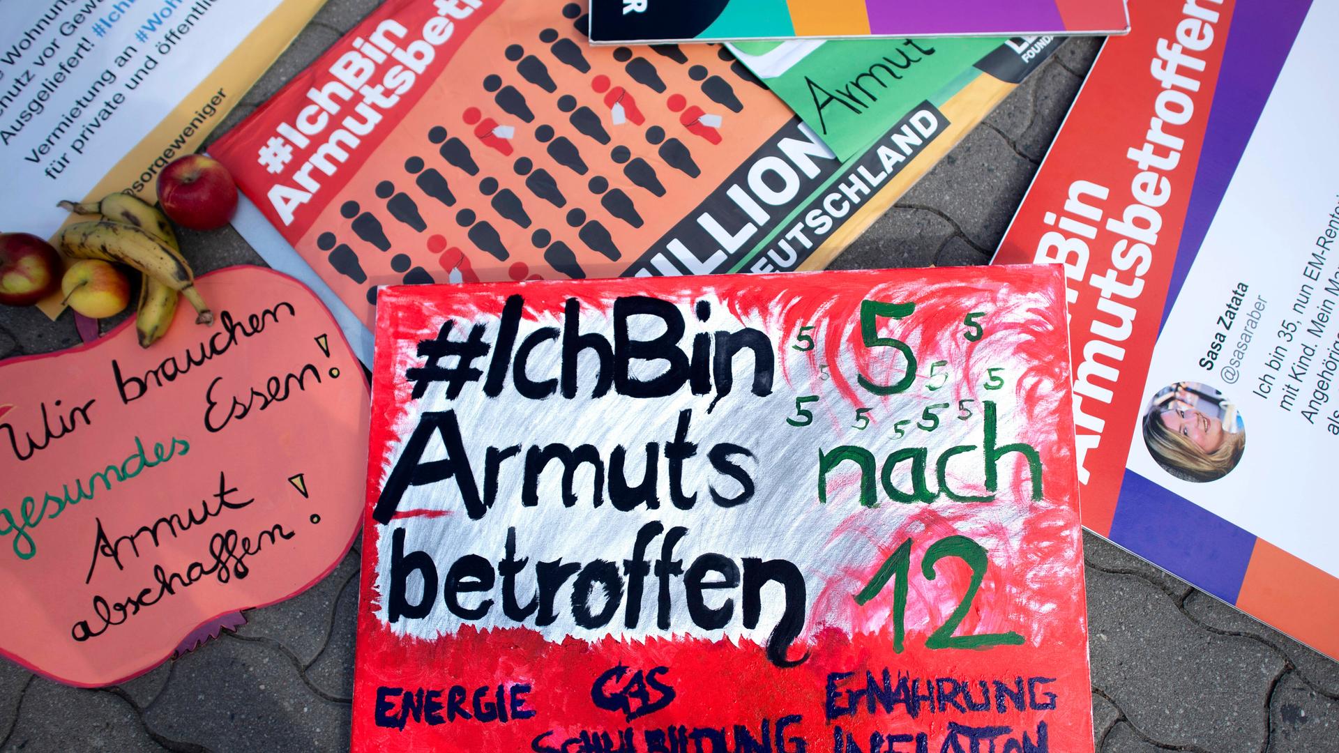 Verschiedene bunte Schilder einer Demonstration liegen auf dem Boden. Auf einem steht "'#IchBinArmutsbetroffen, 5 nach 12", auf einem anderen "Wir brauchen gesundes Essen! Armut abschaffen!"