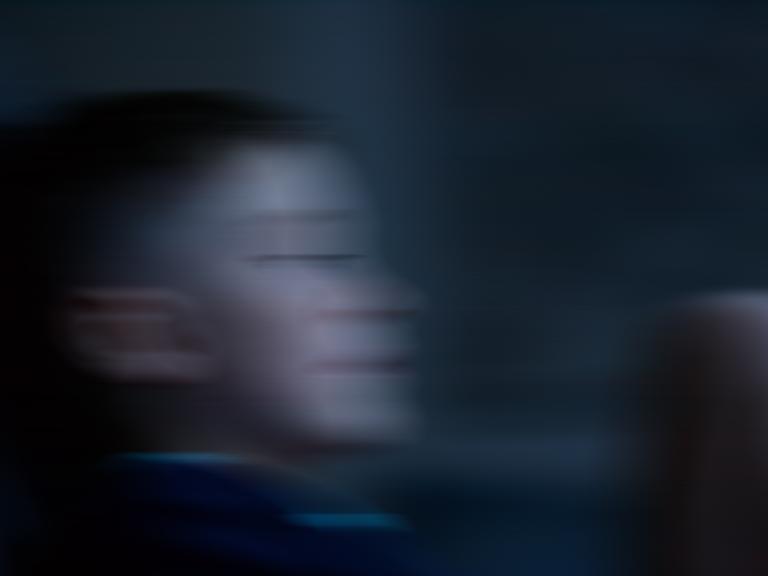 Ein Junge vor dunklem Hintergrund. Das Bild ist mit Bewegungsunschärfe verfremdet.
