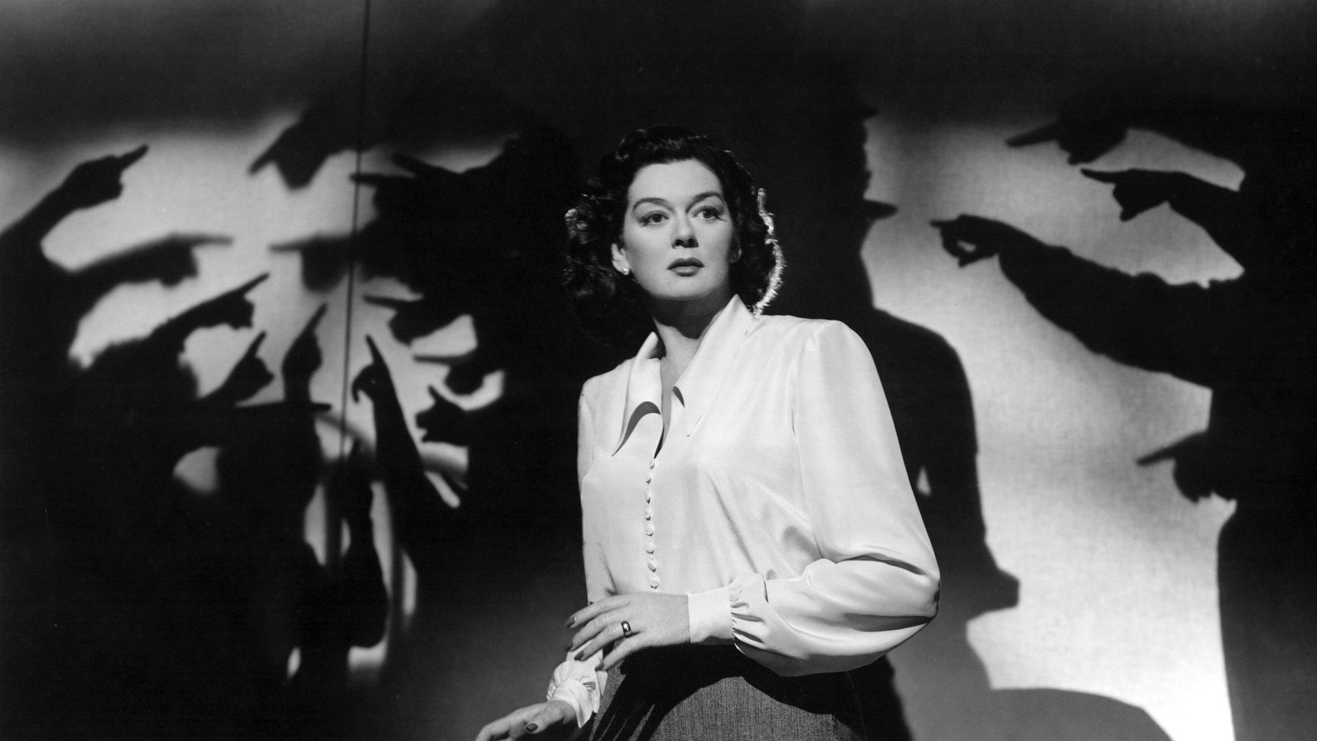 Rosalind Russell in einer Filmszene ca. 1947, in der mehrere Handschatten auf sie zeigen und sie umzingeln. 