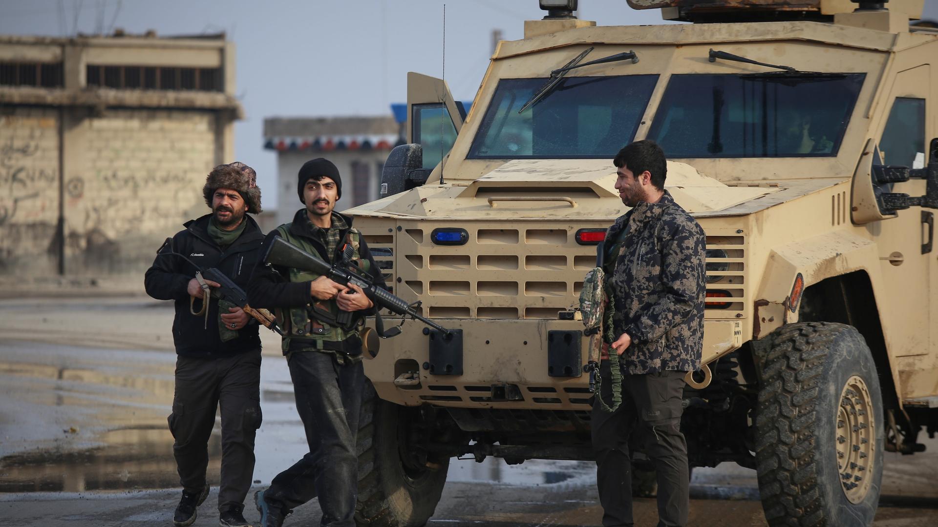 Drei kurdische Kämpfer stehen mit Maschinengewehren in den Händen vor einem Militärfahrzeug.