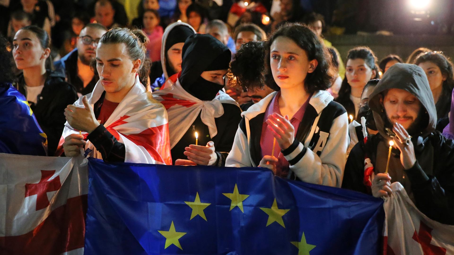 Demonstranten mit georgischen und EU-Fahnen. Die Demonstranten sind junge Menschen. Sie halten Kerzen in den Händen. 