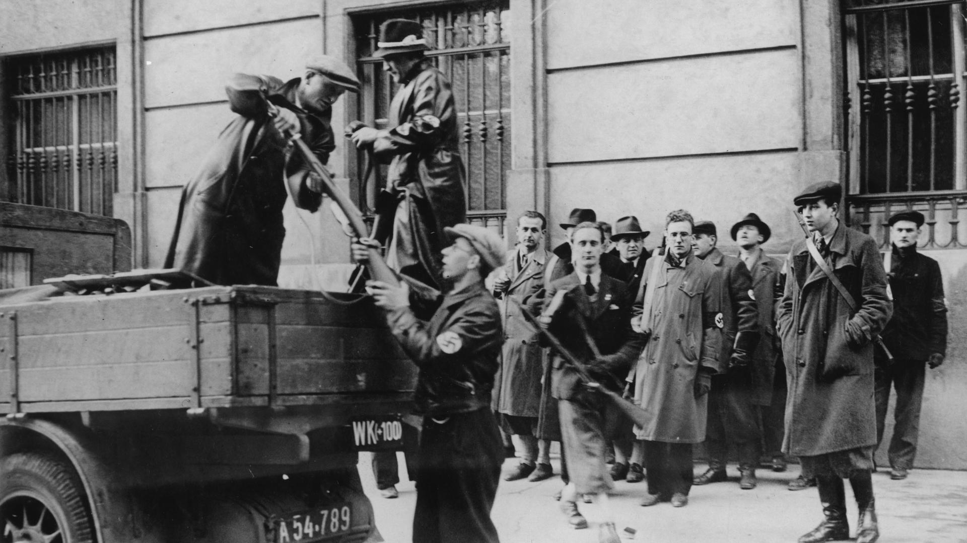 Während des NS-Putschversuchs in Wien am 25. Juli 1934 bewaffnen sich Nationalsozialisten. Ein Mann gibt an andere Waffe nvon einem Fahrzeug aus aus.