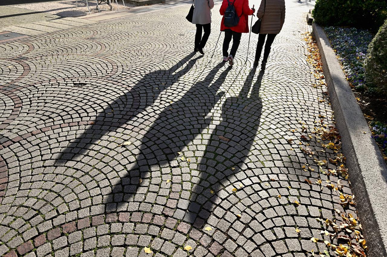 Spaziergang im Herbst. Personen werfen einen malerischen Schatten auf das Kopfsteinpflaster in der Fußgängerzone von Bad Reichenhall. 