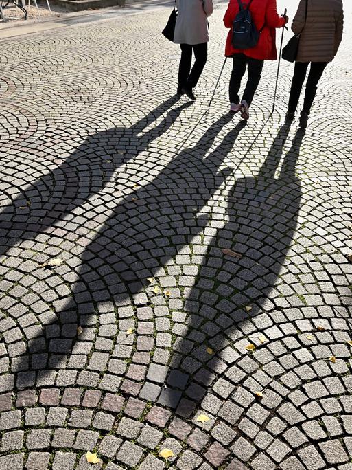Spaziergang im Herbst. Personen werfen einen malerischen Schatten auf das Kopfsteinpflaster in der Fußgängerzone von Bad Reichenhall. 