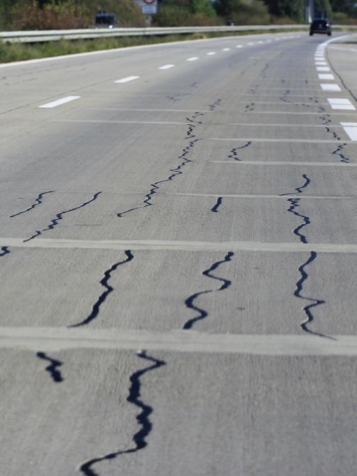 Autobahn mit Rissen in der Fahrbahn, im Hintergrund ein Auto